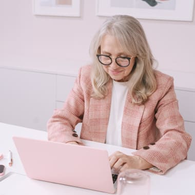 an elderly woman in a pink suit typing on a pink computer on a pink computer