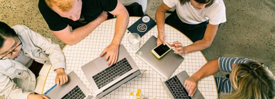 a group of people with macbooks sitting at a desk