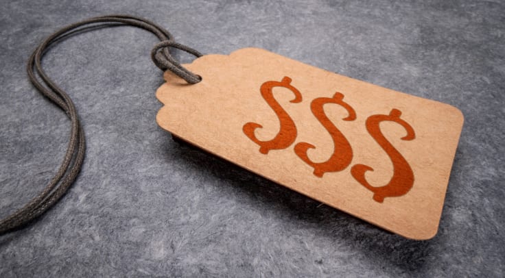 triple dollar sign - red text on a paper price tag against gray paper background, shopping, finance and business concept