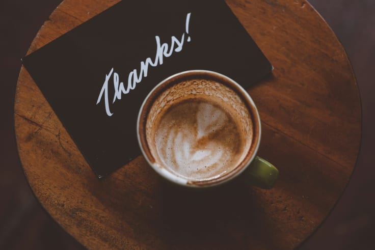 A cup of coffee on a wooden table with a thank you note from an ecommerce store.