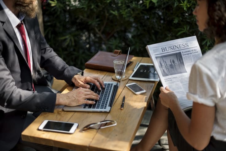 Business people working with laptop reading a newspaper