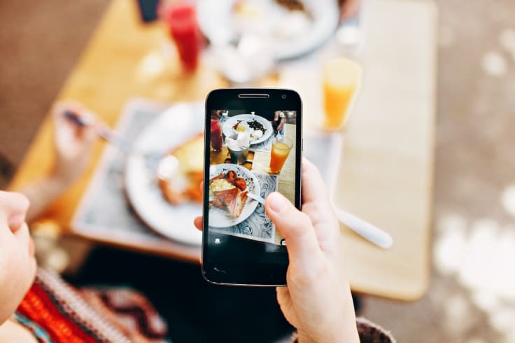 Man holding iphone coffeeshop taking pictures of food