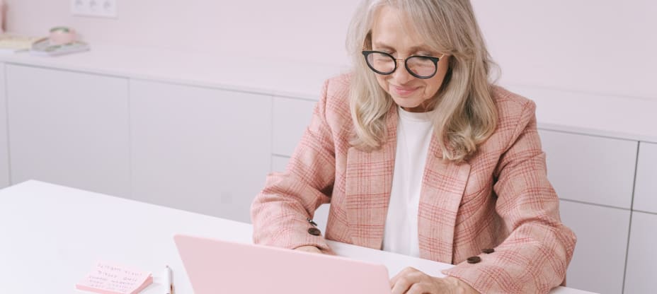 an elderly woman in a pink suit typing on a pink computer on a pink computer