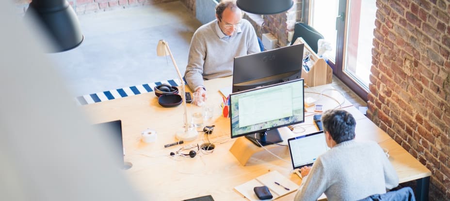 two men sitting in front of computers in an office space