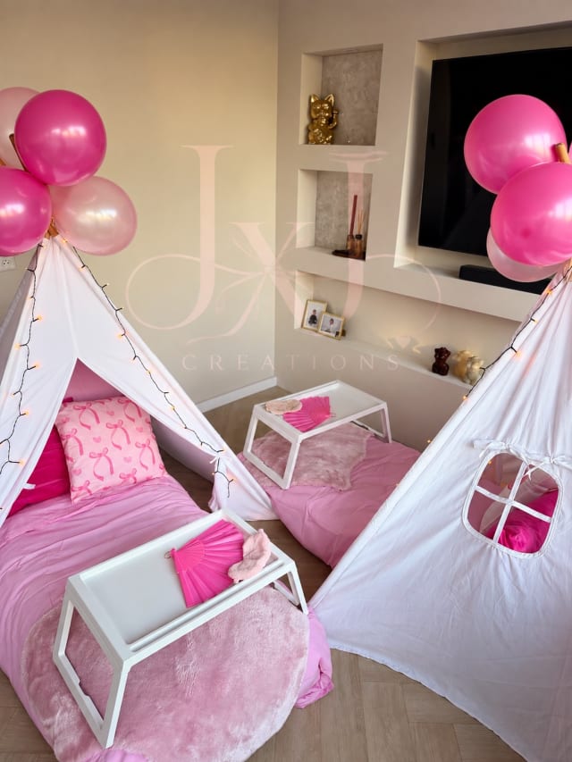 Twee witte tipitenten met roze beddengoed, dienbladen en roze ballonnen
