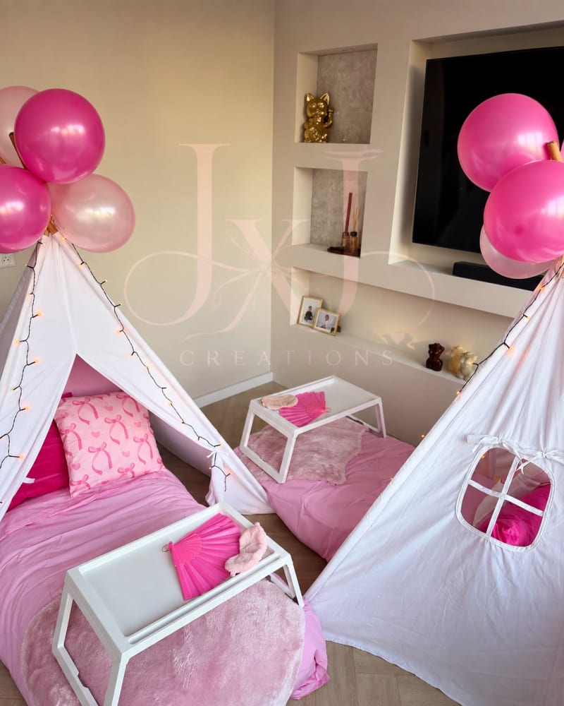 Twee witte tipitenten met roze beddengoed, kussens, dienbladen en ballonnen