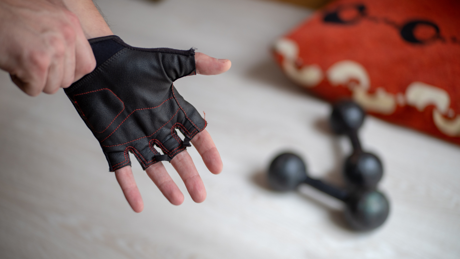 Hand wearing a fingerless leather workout glove reaching toward a set of dumbbells