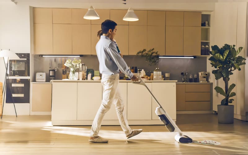 共働きの夫が家事を手伝い、疲れている妻のために掃除機をかけています。家の中は明るく整理されています。