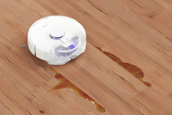 A robot vacuum cleans up a spill on wooden flooring, showcasing useful robot vacuum hacks for effortless cleaning.