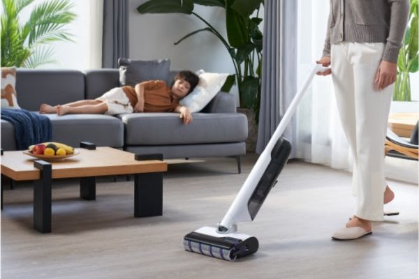 A person uses innovative vacuum cleaners to clean the floor while another relaxes on the couch nearby.