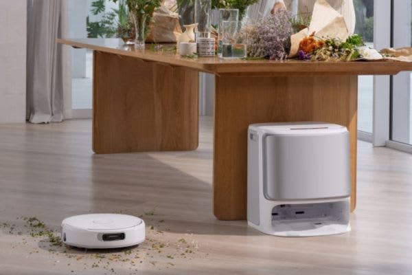 A robot vacuum operates on a hardwood floor beneath a dining table, showcasing how to use robot vacuum on multiple floors.