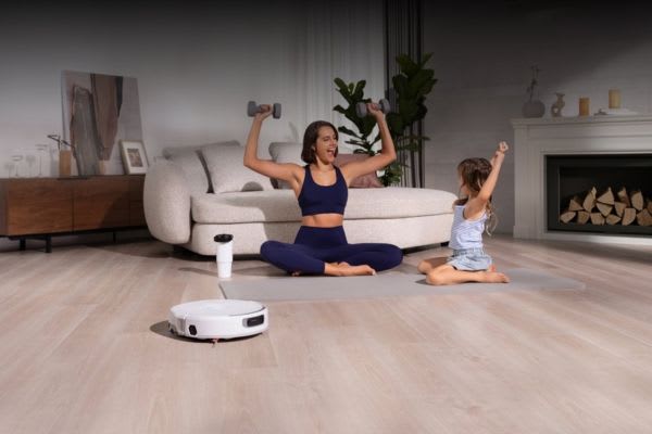 A woman and child exercise together on a mat, while a robot vacuum glides by, wondering if robot vacuums can go over threshold.