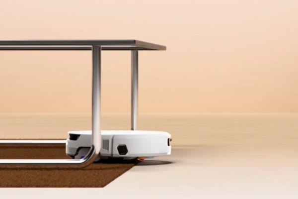 A robot vacuum is approaching a threshold under a table, illustrating the question: can robot vacuums go over threshold?