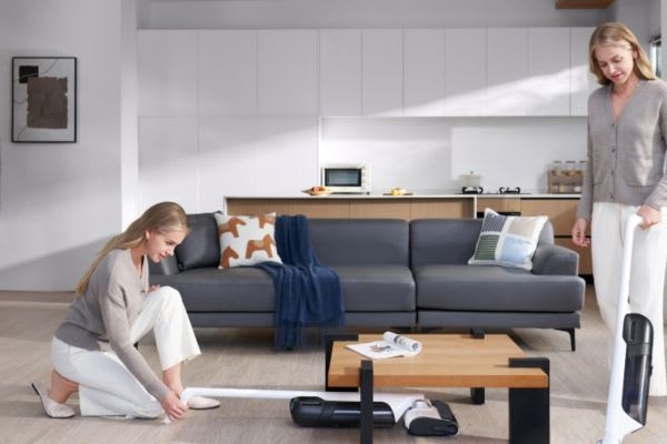 A woman comparing a dust mop vs vacuum while cleaning her modern living room with stylish furniture and a cozy atmosphere.