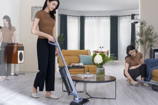 A woman using a vacuum in a modern living room, comparing the efficiency of a dust mop vs vacuum for cleaning.