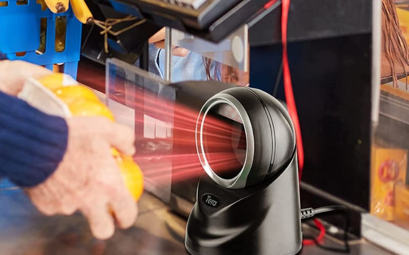 A hand holds a fruit near a presentation scanner, capturing the barcode with a red laser for quick checkout.