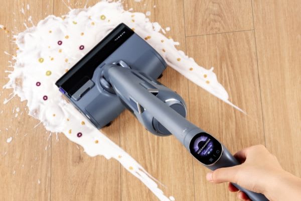 A hand using a vacuum to clean liquid spills, illustrating how to clean vacuum brush roll effectively on a wooden floor.