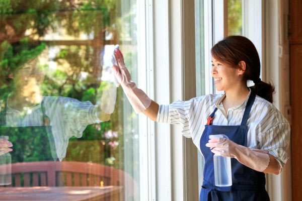 窓を磨いている女性が笑顔で、シルバーウィークの準備をしている様子が描写されています。