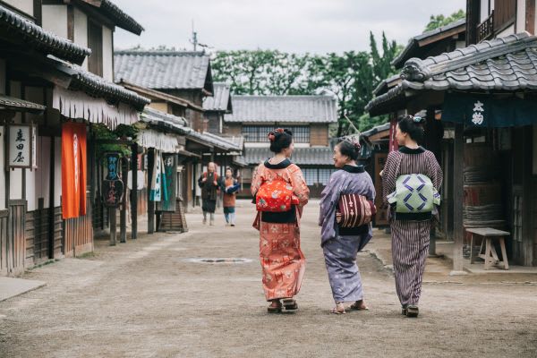 秋の大掃除の前に、伝統的な街並みを訪れる三人の女性が着物を着て歩いています。