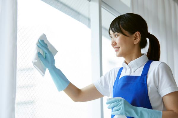 窓を拭いている女性が秋の大掃除をしている様子。清潔感あふれる笑顔で、作業に集中しています。