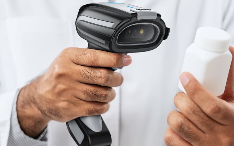 A person holds a barcode scanner in one hand and a pill bottle in the other, emphasizing barcode scanner safety.
