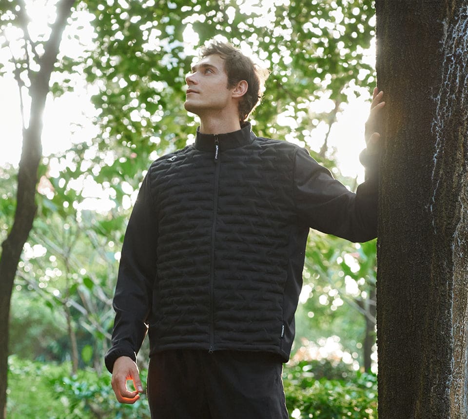 A man in a black jacket stands near a tree, pondering the innovative properties of materials like graphene.