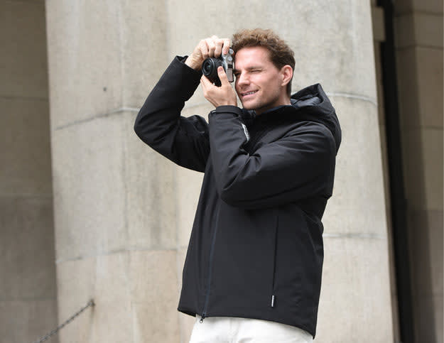A man in a black jacket takes photos, showcasing a versatile choice in the debate of down vs synthetic jacket options.