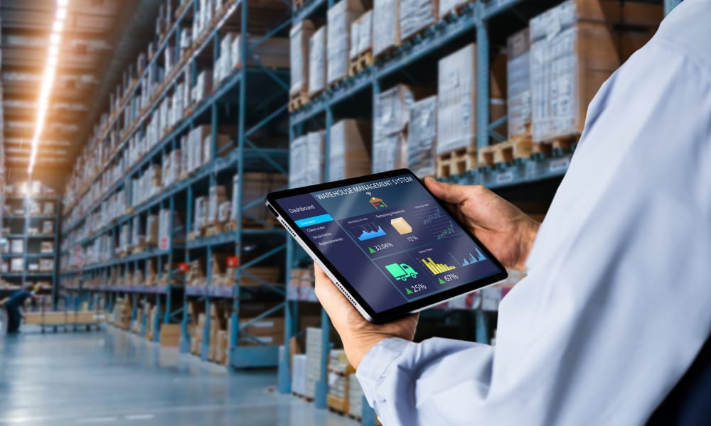 A person using a tablet to monitor warehouse inventory management, enhancing efficiency alongside a retail barcode scanner.