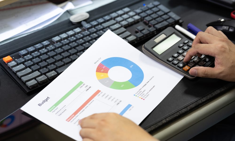 Hands calculating budget figures with a calculator, while a colorful budget report is placed on a keyboard.