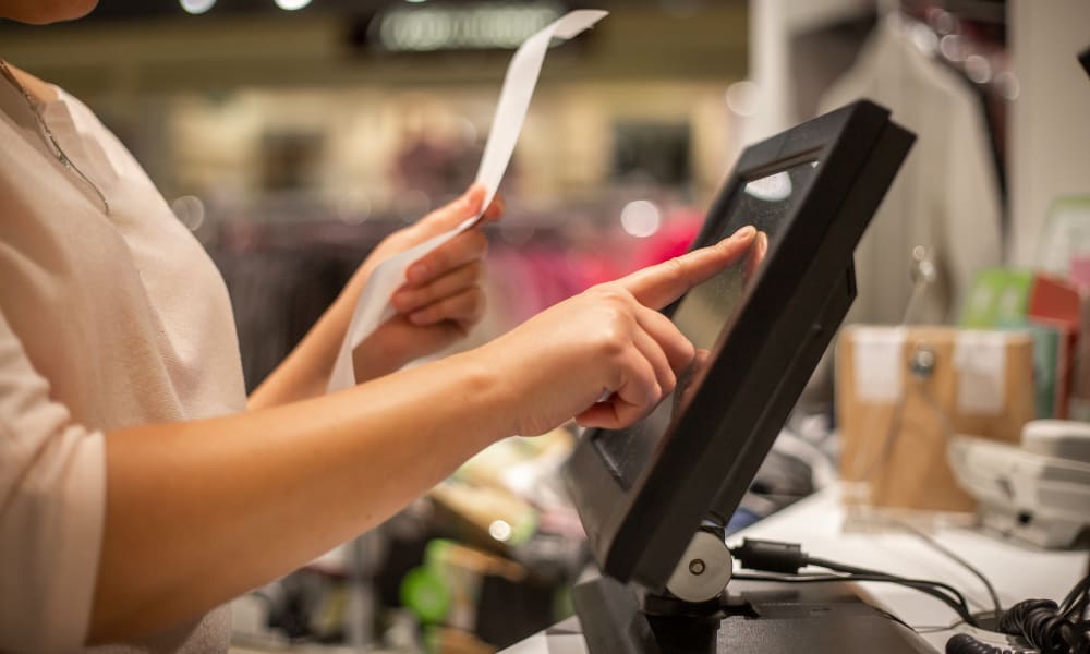 A customer using a retail barcode scanner on a touchscreen device while processing a transaction in a store.