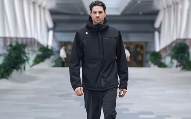 A man wearing a black jacket walks through a modern space, comparing the practicality of hardshell vs softshell jacket options.