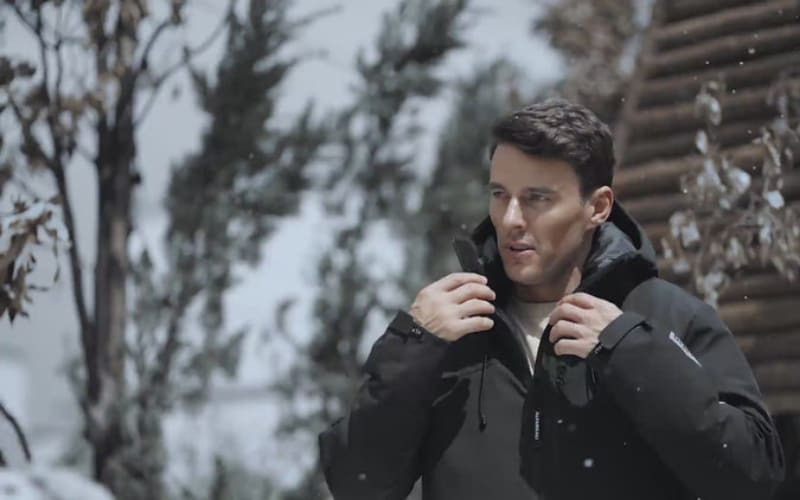 A man adjusts his down jacket in a snowy landscape, debating the choice between down jacket vs puffer jacket for warmth.