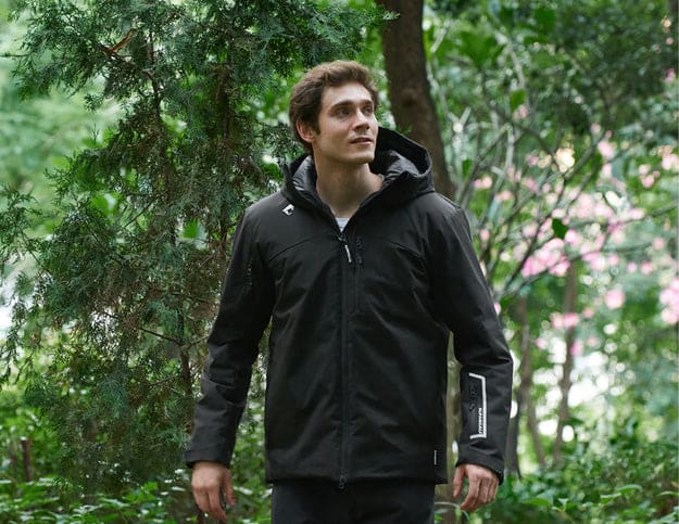 A man in a black jacket stands in a green park, showcasing the style differences between down jacket vs puffer jacket.