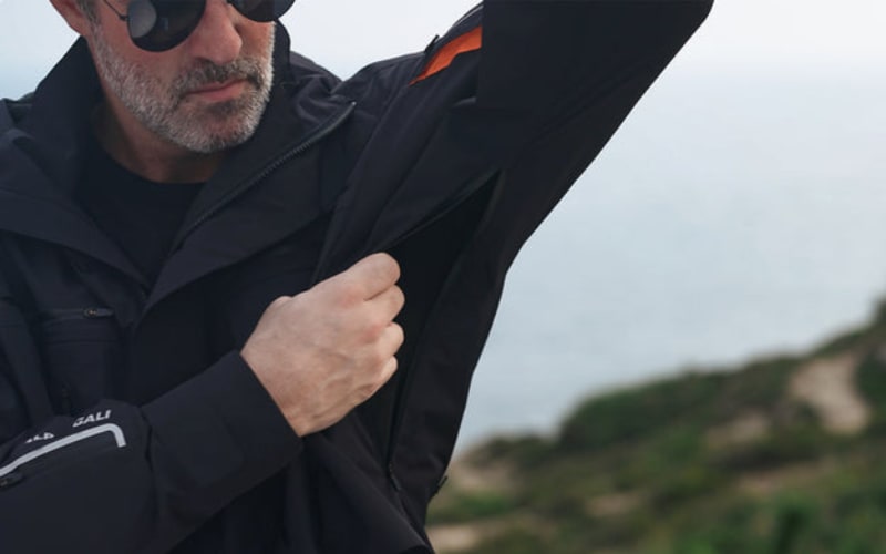 A man inspects his jacket at the coast, comparing features of a shell vs insulated jacket.