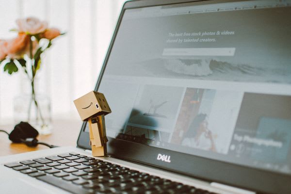 デスクトップの前に小さなロボットが立ち、パソコン画面でamazonの秋セールを探しています。