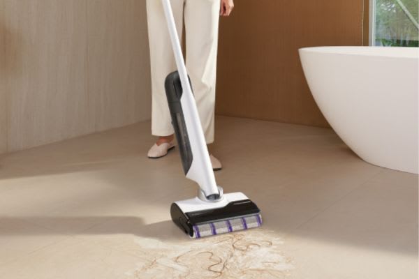 A person using a sleek house cleaning robot to effortlessly clean a tiled floor near a bathtub.