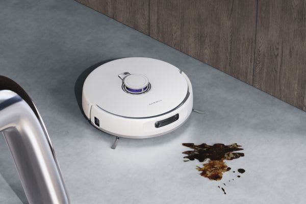 A house cleaning robot is shown on a floor, preparing to clean a mess made by spilled food or liquid.