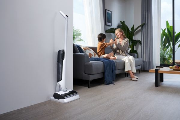A woman and a child enjoy a playful moment at home, while a sleek house cleaning robot stands ready nearby.