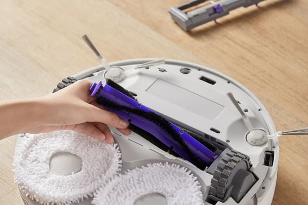 A hand is replacing vacuum attachments in a robotic vacuum, showing the cleaning brush and pads.