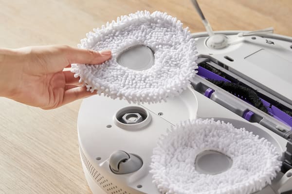 A hand holds soft vacuum attachments, ready to be placed on a cleaning robot for efficient dusting.