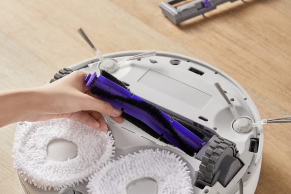 A person is replacing a roller brush in a HEPA vacuum cleaner on a wooden floor.