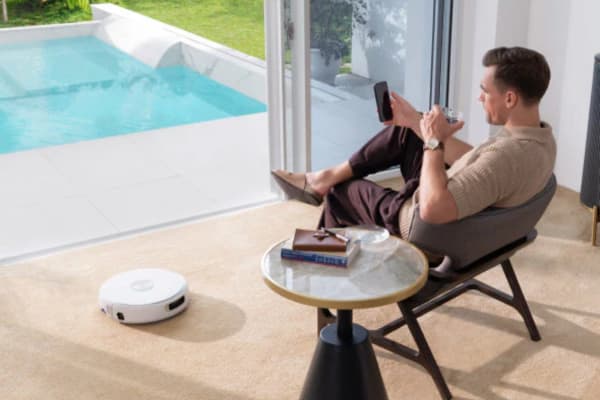 A man relaxes by the pool while a robot vacuum operates nearby, showcasing its efficiency in cleaning.