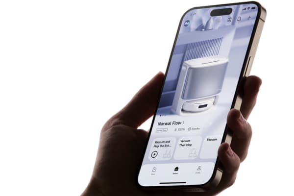 A person holds a smartphone displaying the Narwal Flow robot vacuum, featuring mapping options.