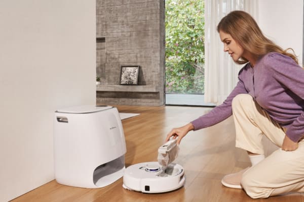 A woman is interacting with a robot vacuum with docking station, maintaining its cleaning component.