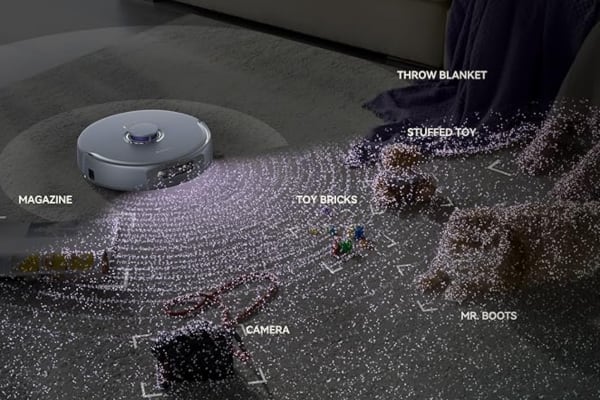 A robot vacuum navigating around scattered toys and a blanket, showcasing compatibility with smart home assistants.