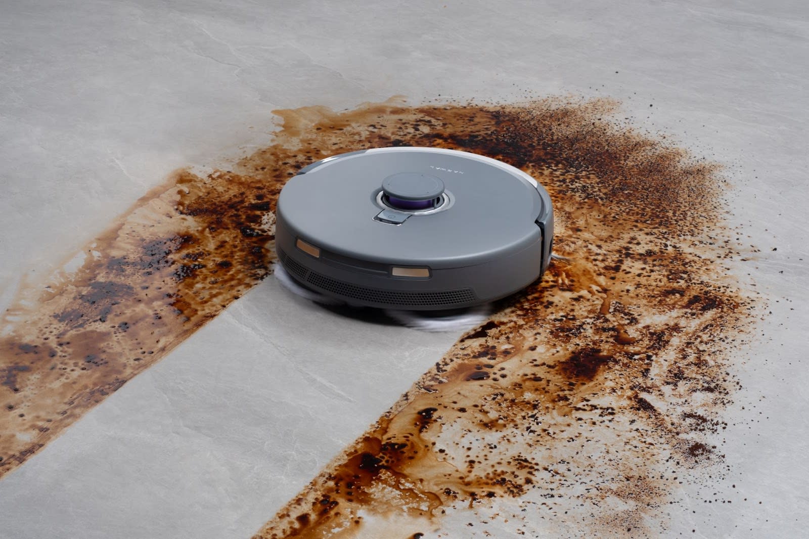 A robotic vacuum cleaning a stained floor, showcasing its flooring compatibility for effective cleaning.