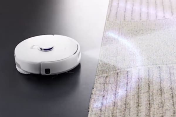 A robot vacuum navigating between a hard floor and a textured rug, demonstrating whether can robot vacuums go over rugs.