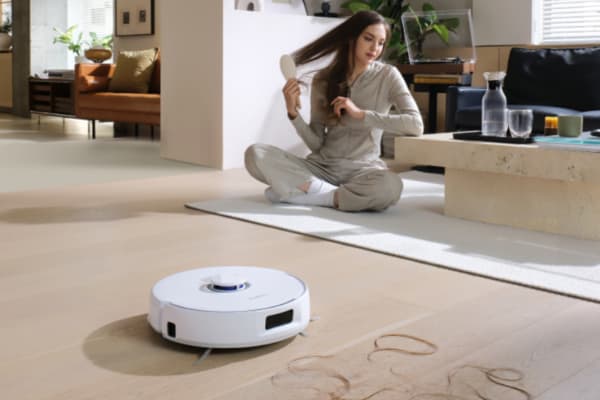 A woman sits on the floor while a robot vacuum cleans nearby, questioning: can robot vacuums go over rugs?