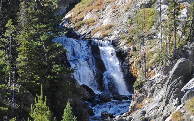 A scenic view of a waterfall surrounded by lush greenery, ideal for yellowstone hikes.