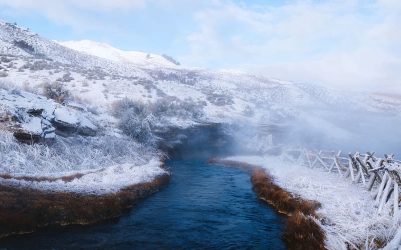 A snowy landscape near a river, showcasing the serene beauty of Yellowstone hikes in winter.